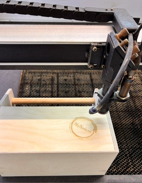 Lasergravur der Putzkiste Liesl in den VARIUS Werkstätten MeNature-Logo wird per Laser auf die Holz-Putzkiste Liesl graviert, VARIUS Werkstätten der Lebenshilfe Rhein-Kreis Neuss